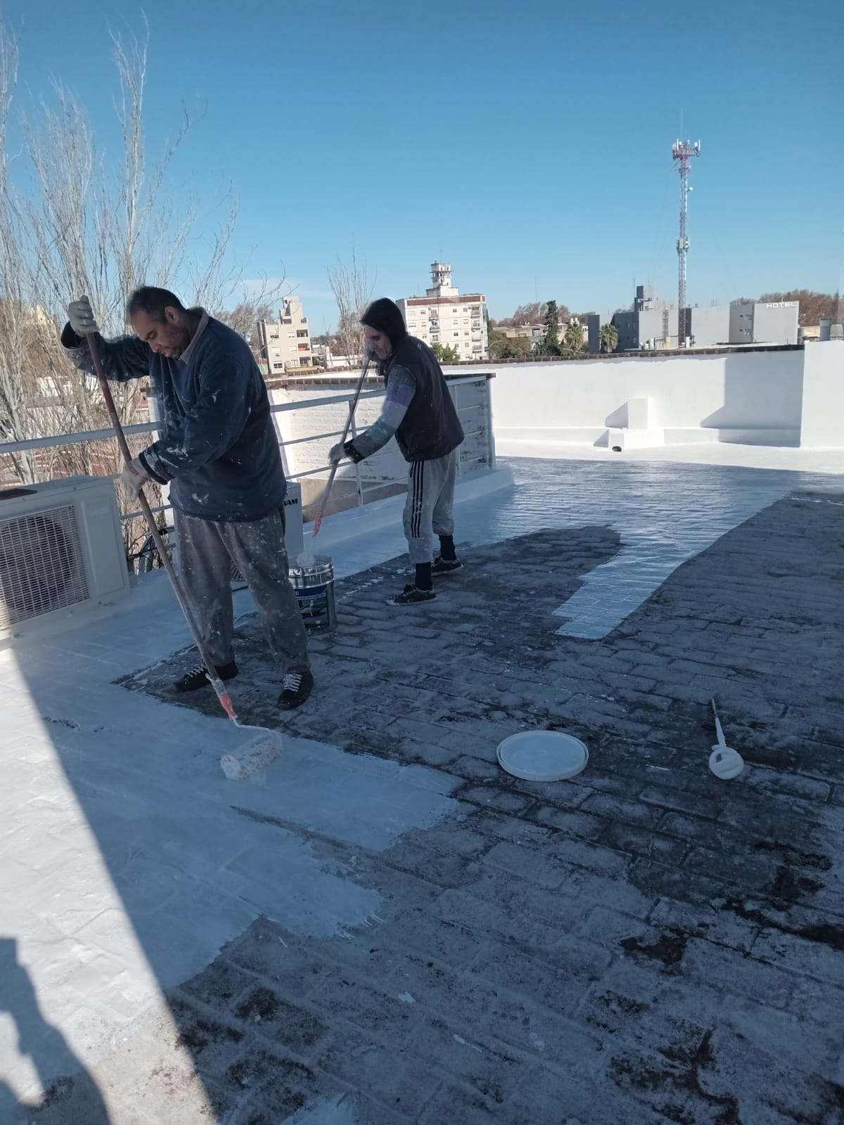 Operarios aplicando membrana impermeabilizante blanca sobre el piso de una terraza